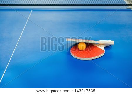 pingpong rackets and ball and net on a blue pingpong table