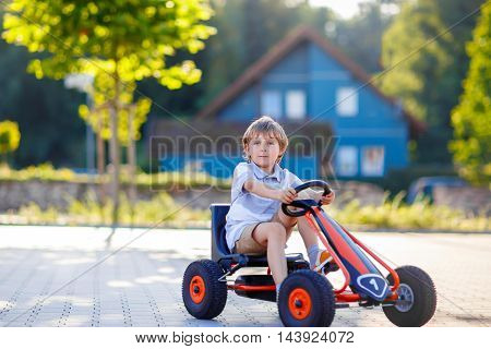 Active little kid boy driving pedal race car in summer garden, outdoors. child racing with fast speed and having fun.