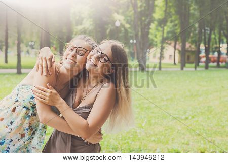 Two happy young girls hug each other. Female friends in eyeglasses embracing, laughing and excited. Woman friendship, walk in the park outdoors