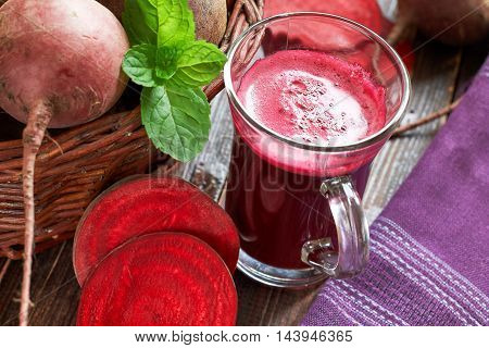 Beetroot juice on wooden background with beetroots and mint leaves in woven basket