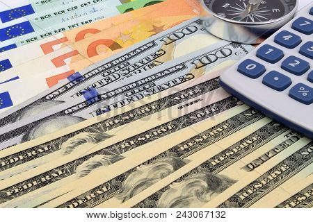 A Close Up Of Euro And Us Dollar Currency Notes With A Caculator And Compass.