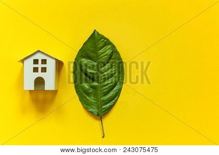 Miniature Toy Model House With Green Leaves On Yellow Colourful Trendy Backgdrop. Eco Village, Abstr