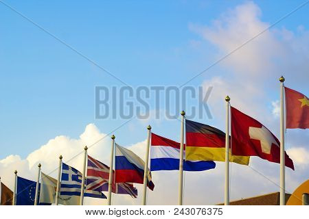 Flags Of Different Countries Flapping In Wind Against Blue Sky