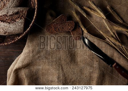 Top View Of Bread Slices, Sackcloth, Knife And Wicker Breadbasket On Wooden Table