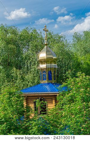 Wooden Orthodox Church With Gilded Domes On A Background Of Green Foliage Of Trees And A Bright Blue