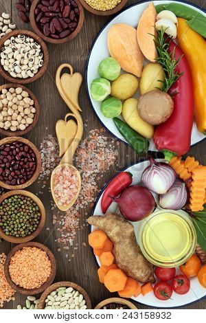 Food for health and well being concept with fresh vegetables, herbs, dried pulses, himalayan salt and olive oil.  Foods high in antioxidants, fibre, anthocyanins and vitamins.