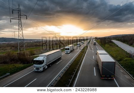 Caravan Or Convoy Of White Trucks In Line On A Country Highway At Sunset