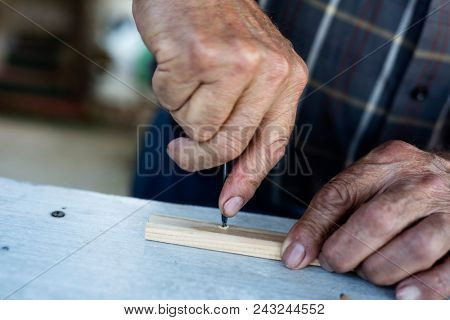 closeup of an old caucasian man making a hole in a wood strip with a gimlet
