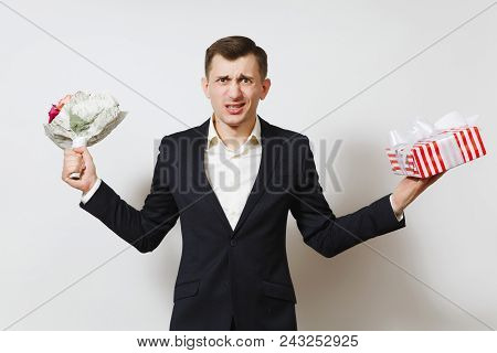 Young Crazy Angry Perturbed Man In Suit Holding Bouquet Of Roses Flowers, Red Present Box With Gift 