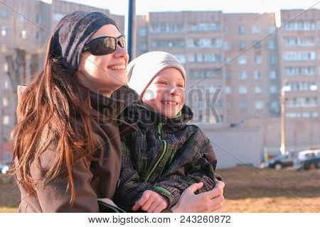 Mom And Son Look Around, And Laugh And Talk Sitting On A Bench In The Park In The Spring