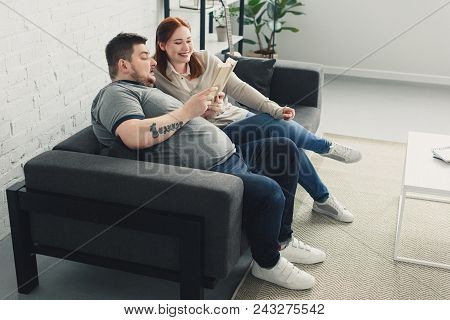 Boyfriend And Girlfriend Reading Book Together On Sofa At Home