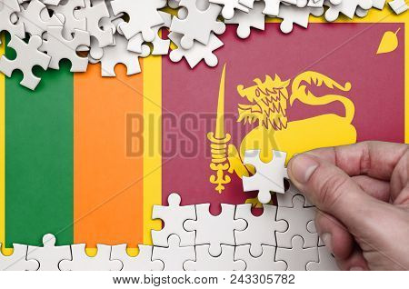 Sri Lanka Flag  Is Depicted On A Table On Which The Human Hand Folds A Puzzle Of White Color.