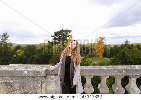 Smiling Girl Standing Near Concrete Railing With Green Trees Background. Concept Of Architectural El