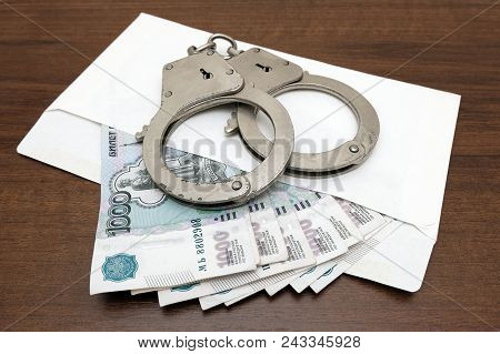 A Bundle Of Russian Rubles A White Envelope And Handcuffs On A Brown Background. The Concept Of Viol