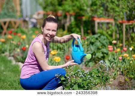 Smiling Caucasian Woman Watering Flowers With Water Can On A Croft.