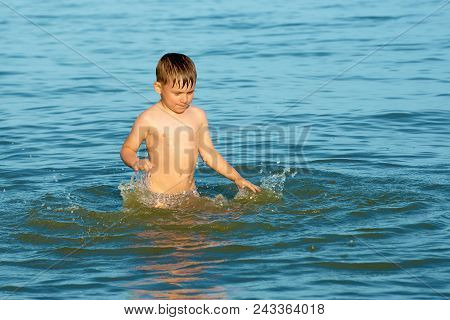 The Boy Sprinkles In The Sea Water On The Ocean On A Summer Day And Waving His Arms In The Direction