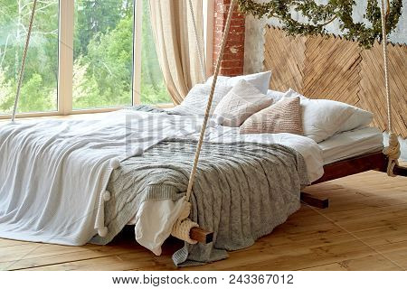 Hanging Wooden Bed Suspended From Ceiling With Pillows And Cozy White Plaid And Knitted Blanket Near