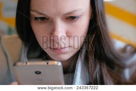 Young Seriously Woman Reading Something On Her Mobile Phone Sitting In Cafe. Closeup Face
