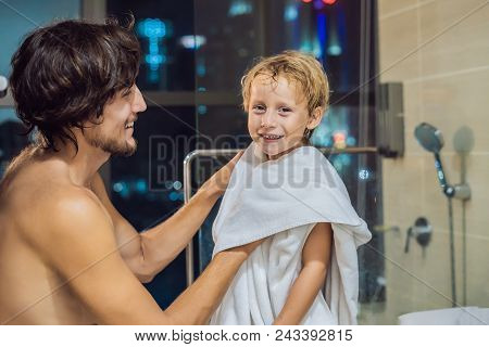 Dad Wipes His Son With A Towel After A Shower In The Evening Before Going To Sleep On The Background