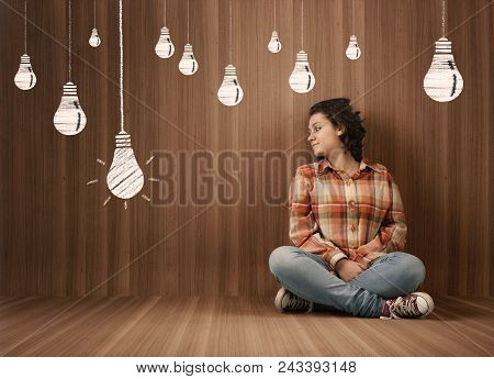 Young Woman Sits In  A Wooden Room And Looks At A Drawn Lightbulb.