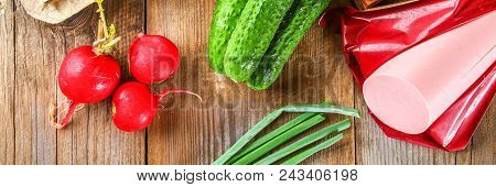 Ingredients For Okroshki - Sausage, Eggs, Radishes, Onions, Potatoes, Cucumbers On An Old Wooden Tab