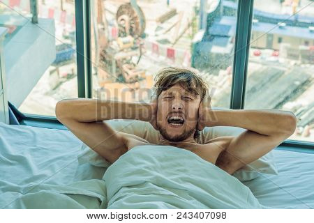 Young Man Lying On A Bed Covered Her Ears Because Of The Noise. In The Window After The Bed You Can 