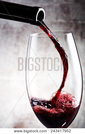 Pouring Red Wine Into The Glass Against Wooden Background