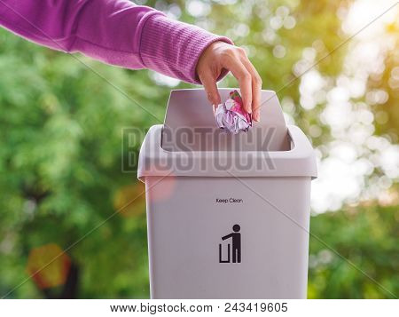 Female Hand Trowing A Paper Into A Garbage Bin On Bokeh Background. Cleaning Concept.