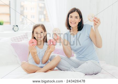 Horizontal Shot Of Beautiful Brunette Femle With Bobbed Hairstyle, Dressed In Pyjamas, Sits Near Her