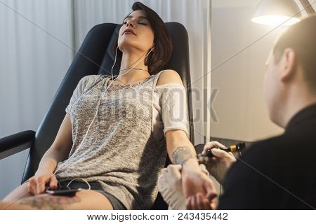 A Professional Tattooer Artist Doing Picture On Woman Hand By Machine While Girl Listening Music. Ta