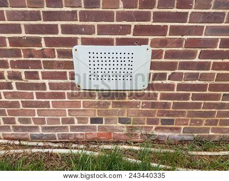 A Metal Vent With Holes On A Red Brick Wall