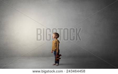 Little waggish kid staying alone in a big empty room with his plush