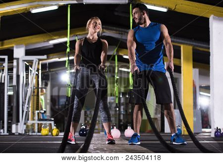 young fit sports couple working out in functional training gym doing  battle ropes cross fitness exercise