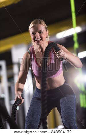 young fit athlete woman working out in functional training gym doing  battle ropes exercise as part of cross fitness training