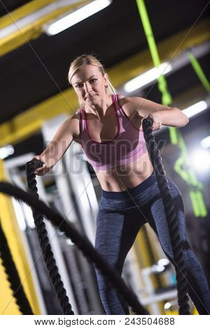 young fit athlete woman working out in functional training gym doing  battle ropes exercise as part of cross fitness training