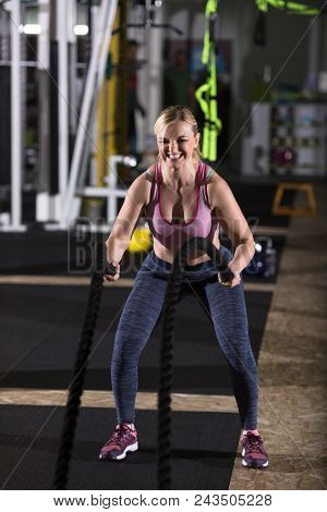 young fit athlete woman working out in functional training gym doing  battle ropes exercise as part of cross fitness training