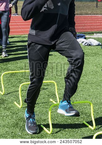 A High School Athlete In A Black Sweatsuite Is Stepping Over Yellow Mini Banana Hurdles During Speed
