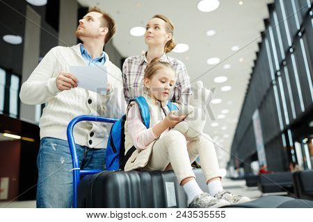 Young couple looking at tableau while moving towards entrance to platform with their daughter sitting on baggage
