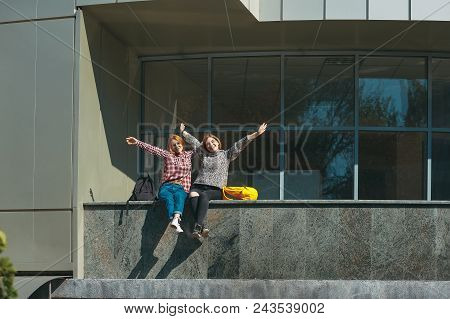 College Students Happy To Finish The Exams. Young Girls With Reddish Hair Sit On A Modern Building N
