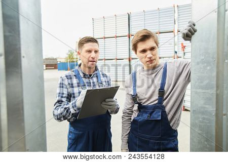One of workers making notes in document while looking at cargo in storage container