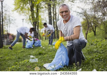Help Planet. Optimistic Senior Volunteer Holding Garbage Bag And Gazing At Camera