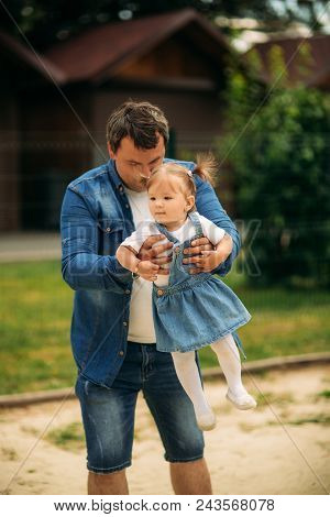 Dad And Daughter Dressed In Jeans Walking In The Pakr And Have Fun.