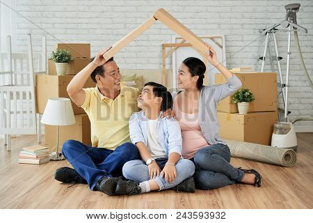 Joyful Asian Family Making Roof From Cardboard Box Over Their Heads And Looking At Each Other With W
