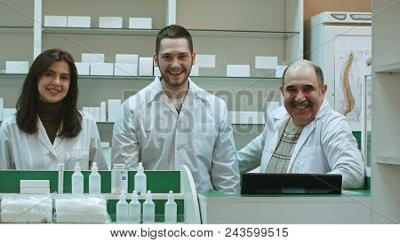 Three Competent Pharmacists Laughing In A Pharmacy Looking At Camera