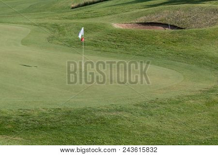 White Flagstick In Green Golf Course In Sunny Day.