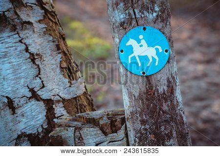 Bridle Path Round Blue Sign On A Wooden Stake, With Blurry Land Path In The Background. Germany.