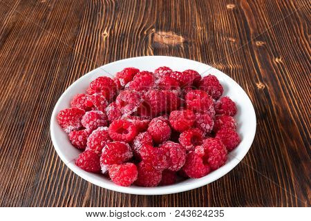 Deep Frozen Red Raspberry Berries For Long-term Storage In A White Plate On A Brown Wooden Table