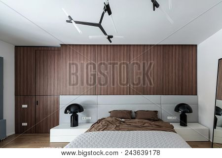 Contemporary Bedroom With White Walls And A Parquet On The Floor. There Is A Bed With A Brown Linens