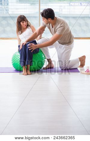 Personal coach helping woman in gym with stability ball