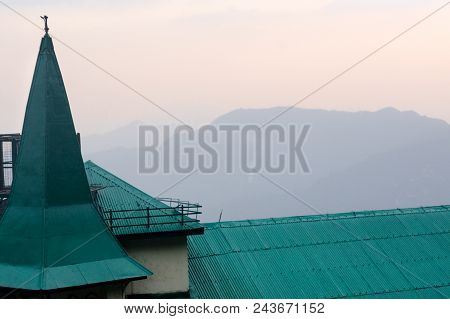 Green Roof And Tower Of A House Set Against The Blue Hills And Pink Sky Of A Beautiful Dusk . Shot I